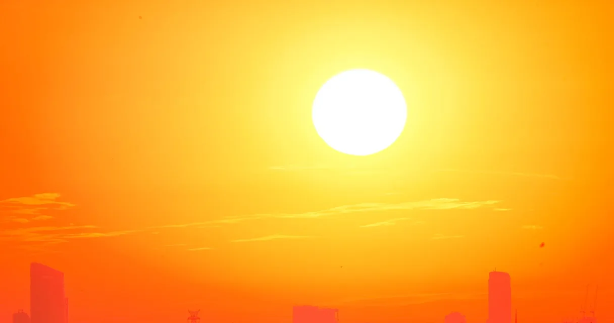 Sol forte em um céu alaranjado sobre a silhueta de uma cidade, ilustrando o calor nos eletrônicos