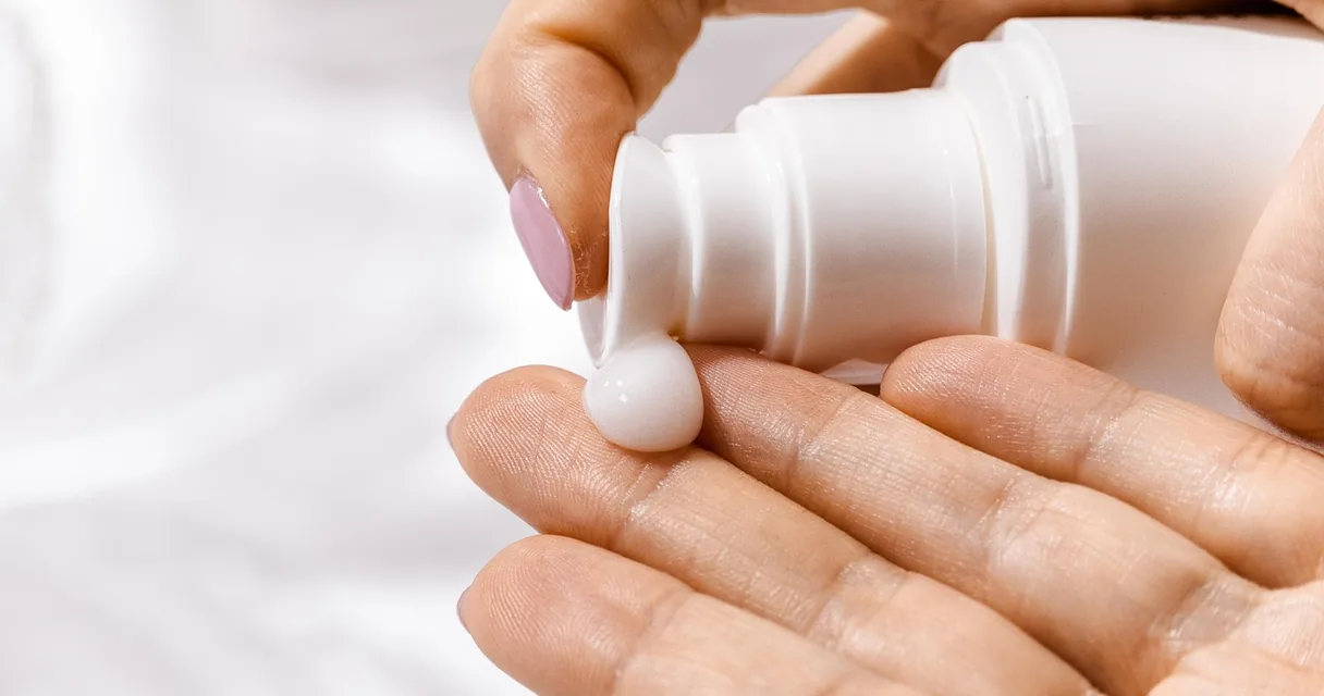 Mão aplicando creme hidratante de um frasco